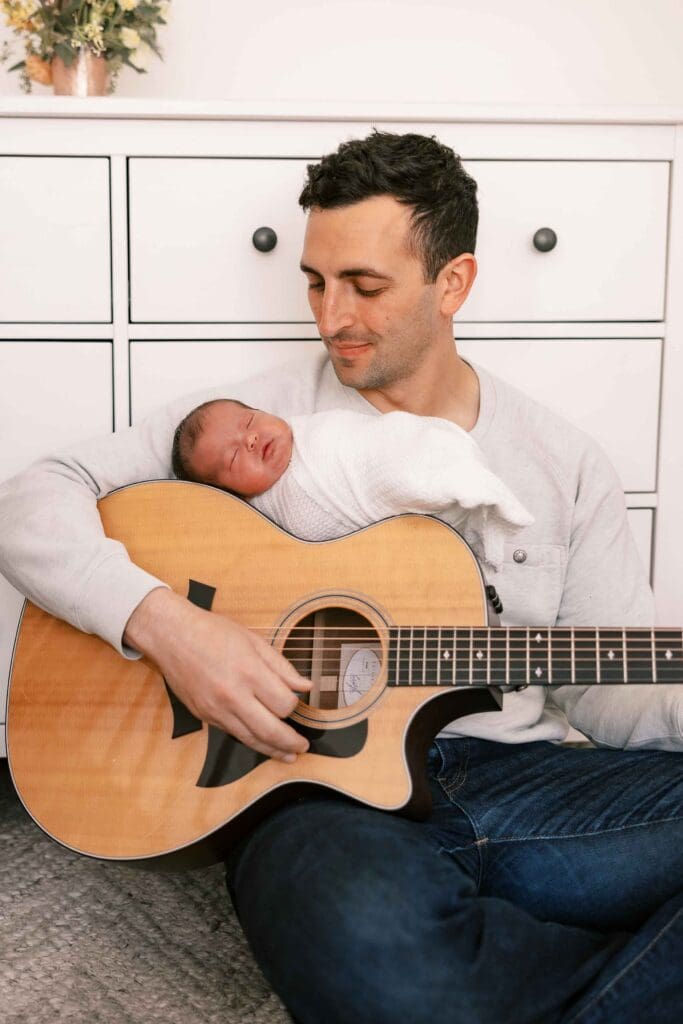 Dad playing guitar with baby sleeping on top