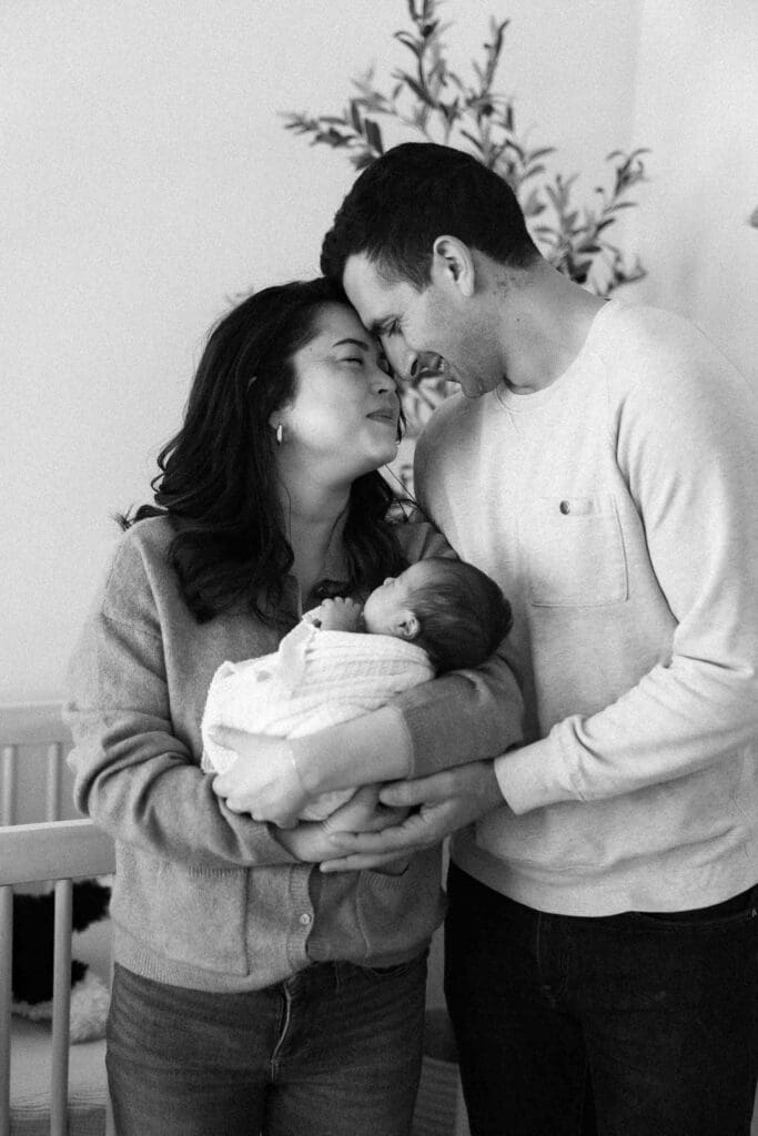 New mom and dad snuggling each other and holding their newborn baby girl