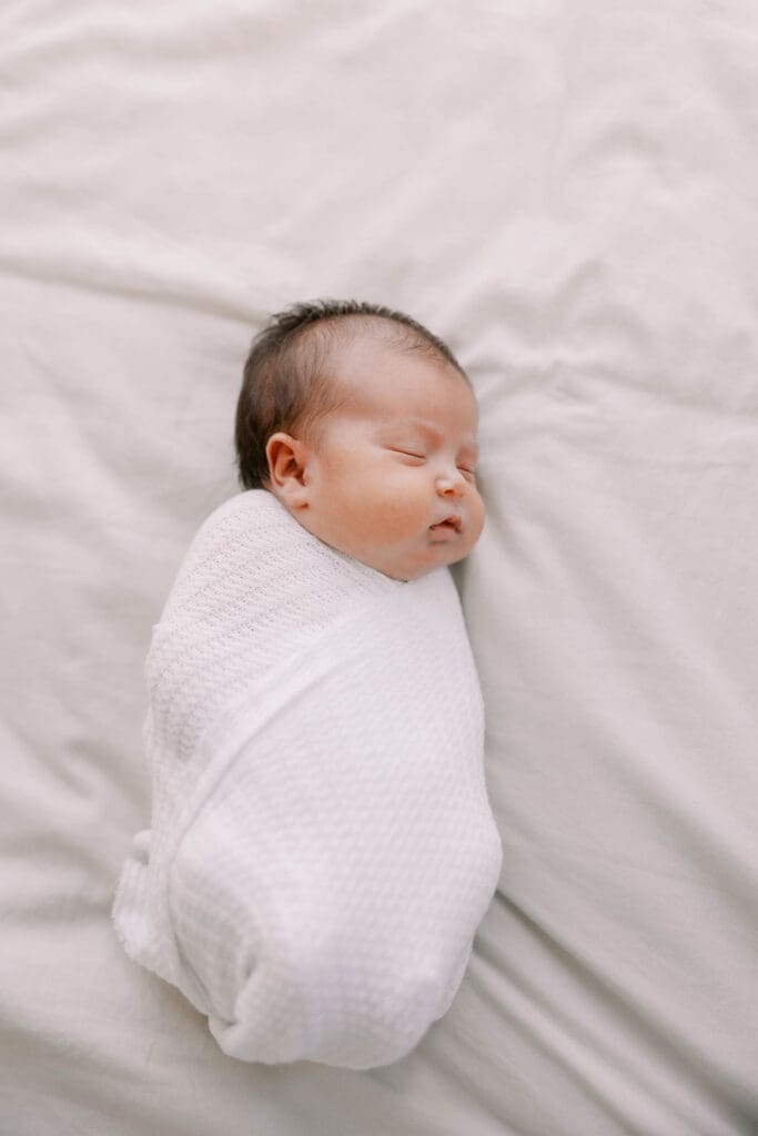 Newborn baby girl wrapped in a white swaddle and laying on a blanket
