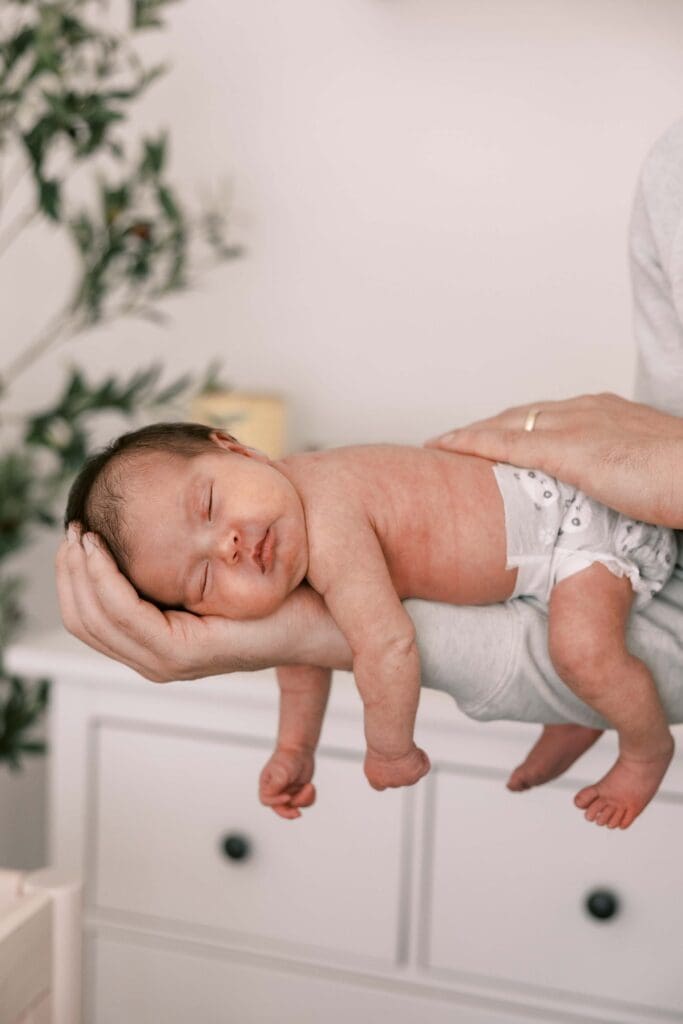 Dad holding newborn baby girl on his arm with her head in his hand in their San Francisco apartment