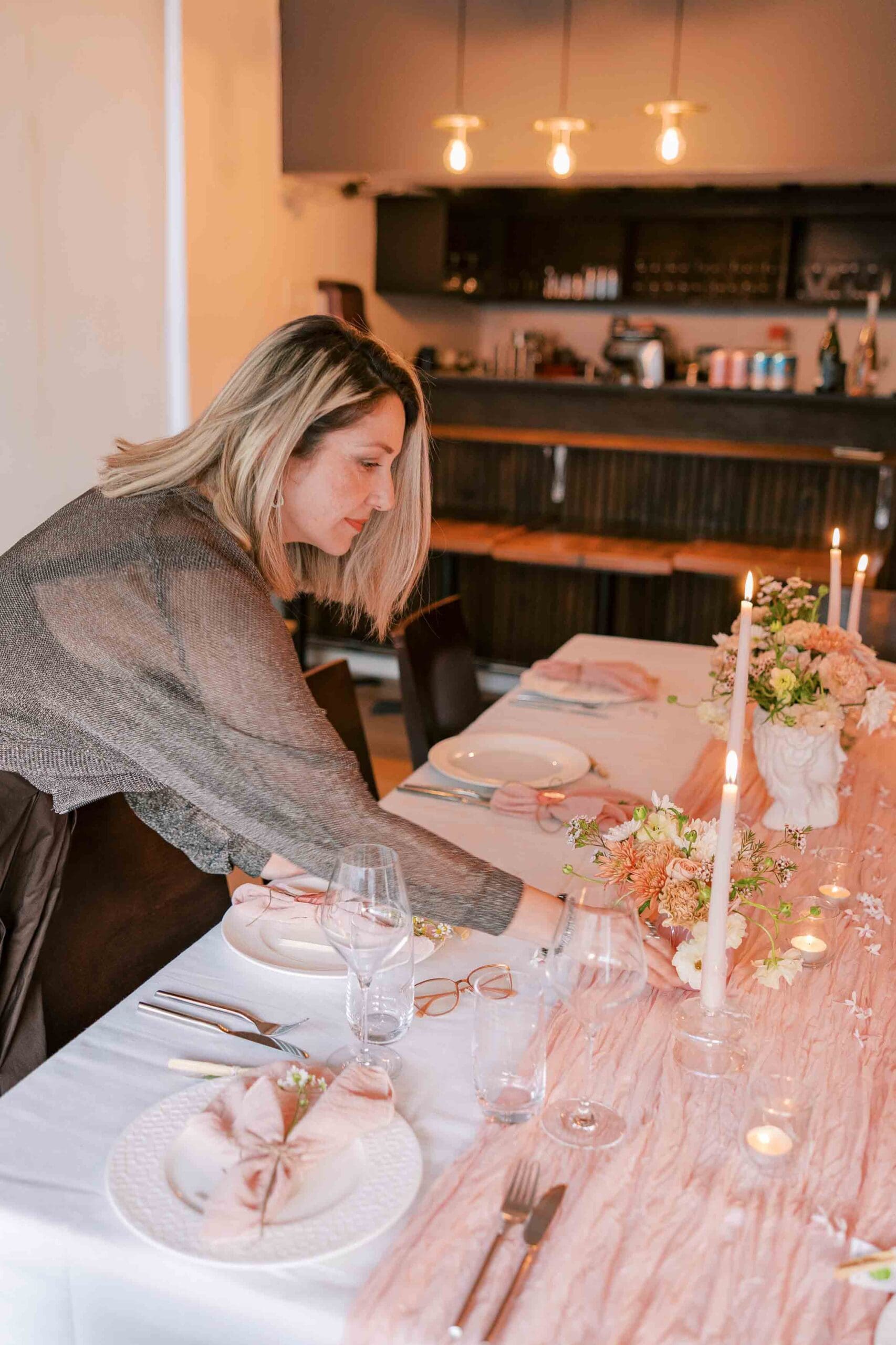 Blonde woman wearing a brown dress and sheer cardigan, setting the table