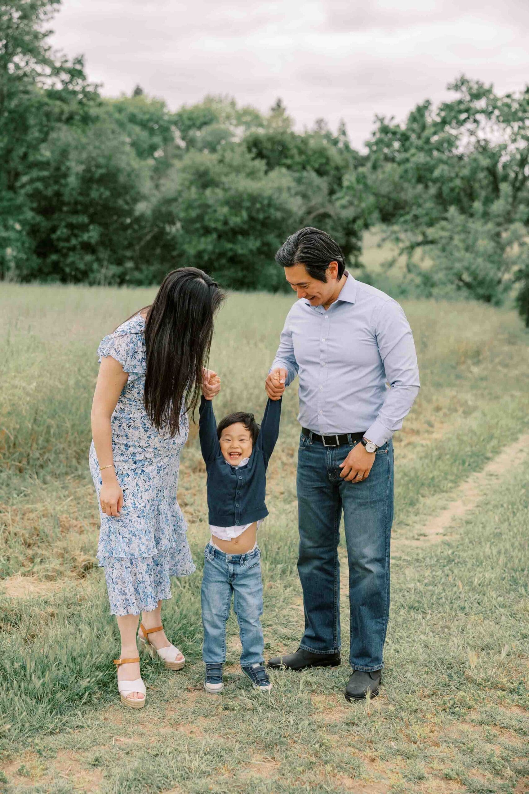 Parents swinging child by his arms in a field of green