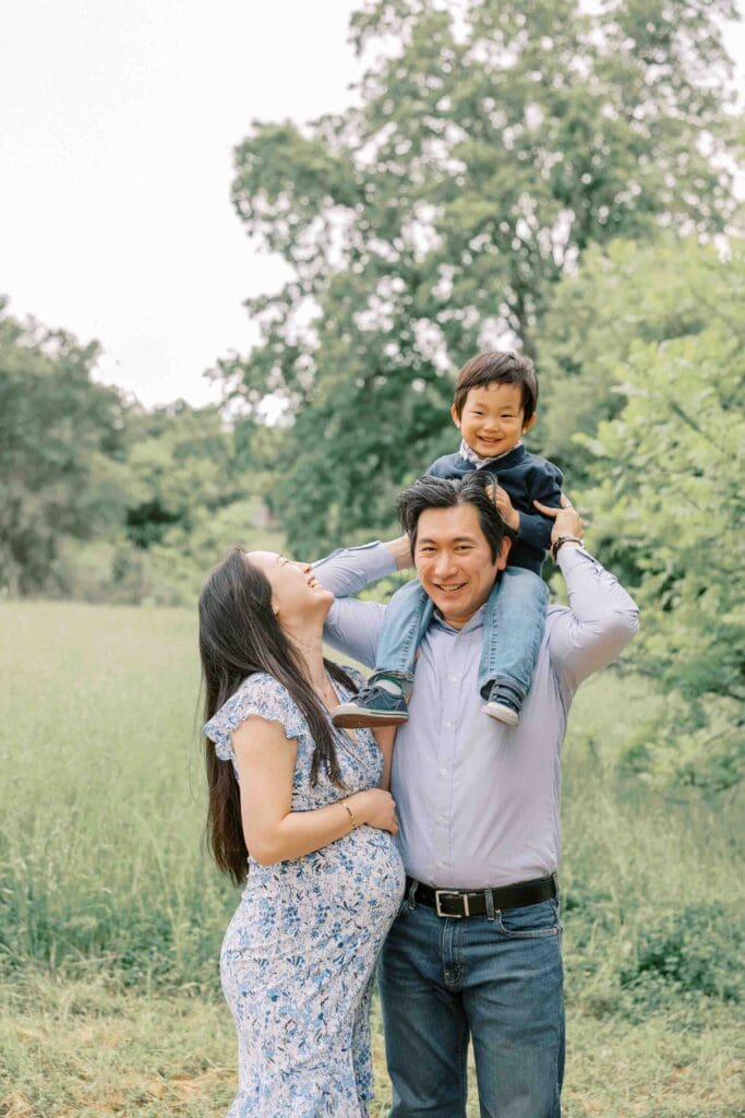 Little boy on dad's shoulders with pregnant mom looking at him and beaming