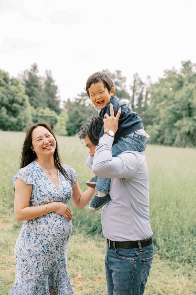 Little boy on dad's shoulders with pregnant mom looking at the camera and beaming
