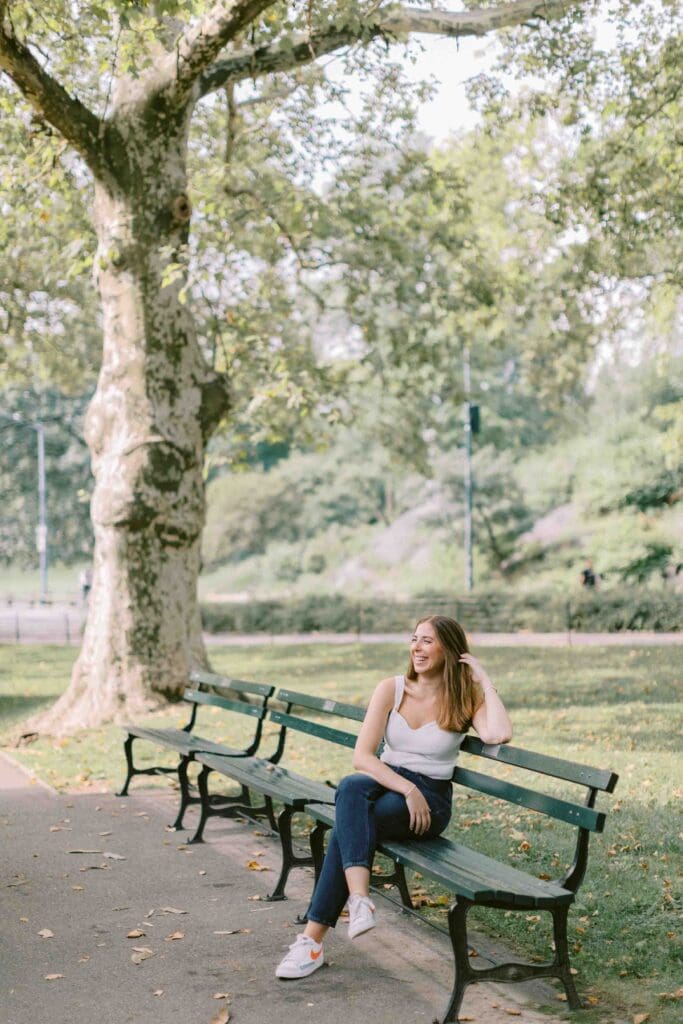 Woman sitting on a green park bench and laughing while looking out into the distance for her dating profile photo