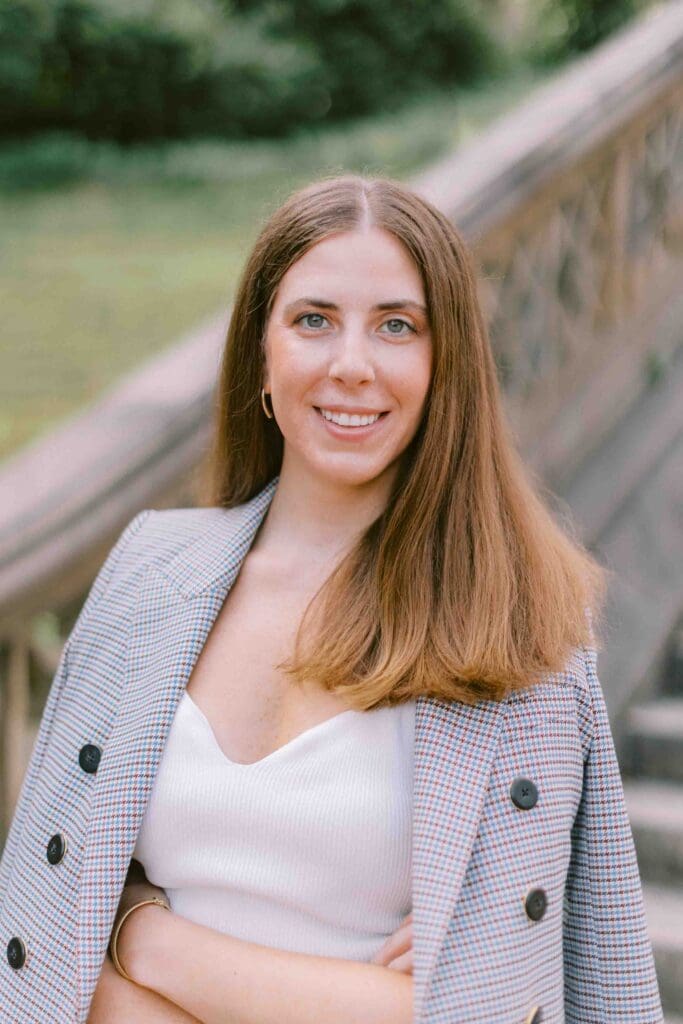 Woman wearing a checkered blazer, crossing her arms, and smiling at the camera for a dating profile photo