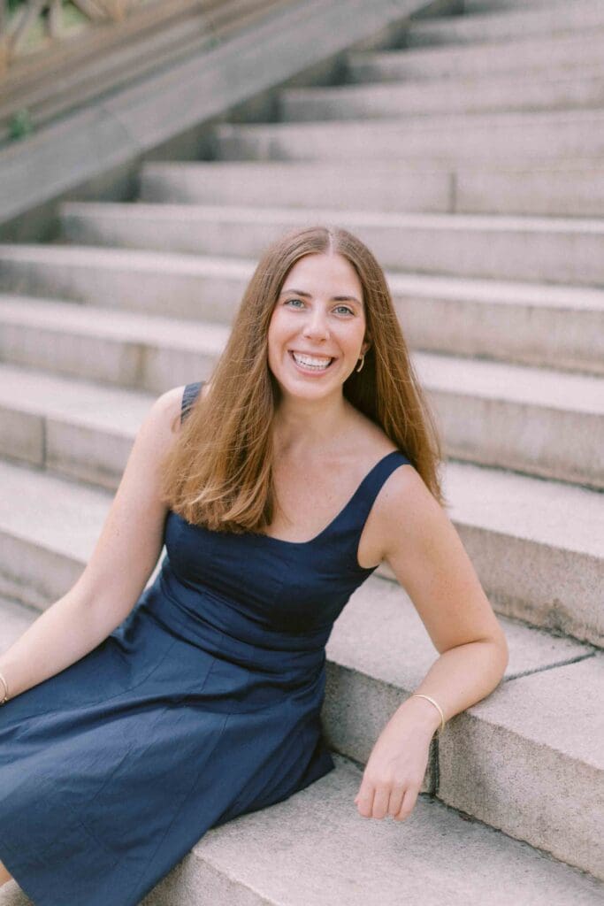 Woman wearing a navy blue skater dress and sitting on marble steps, smiling at the camera
