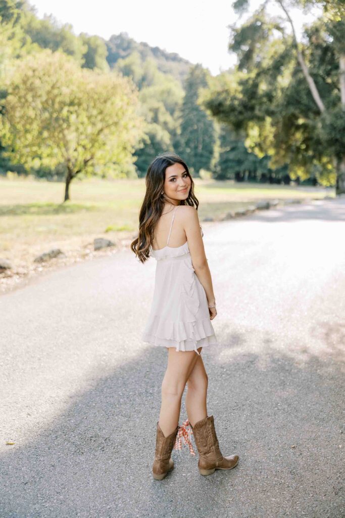 Brunette girl wearing a white dress and cowboy boots and looking back over her shoulder