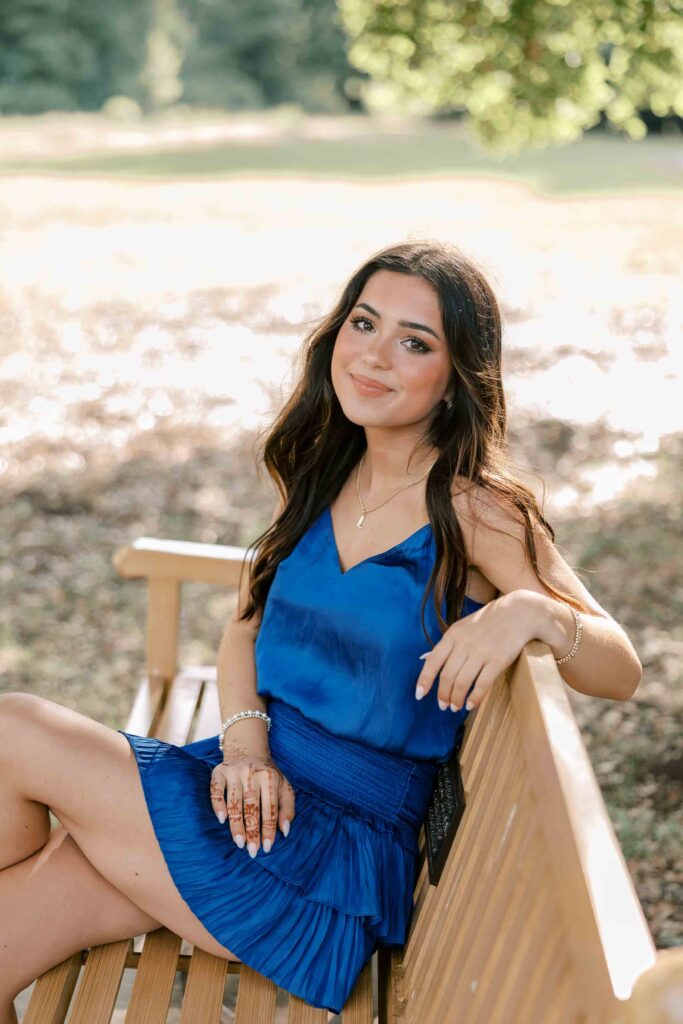 Brunette girl wearing a royal blue dress and sitting casually on a park bench