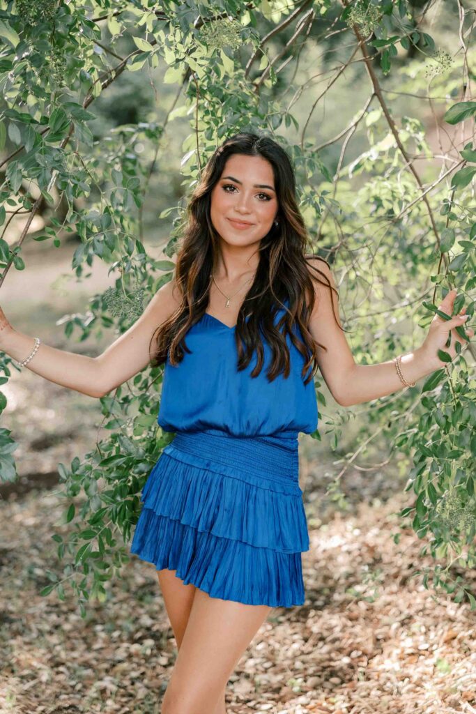 Brunette girl wearing a royal blue dress and peeking through an oak tree's branches