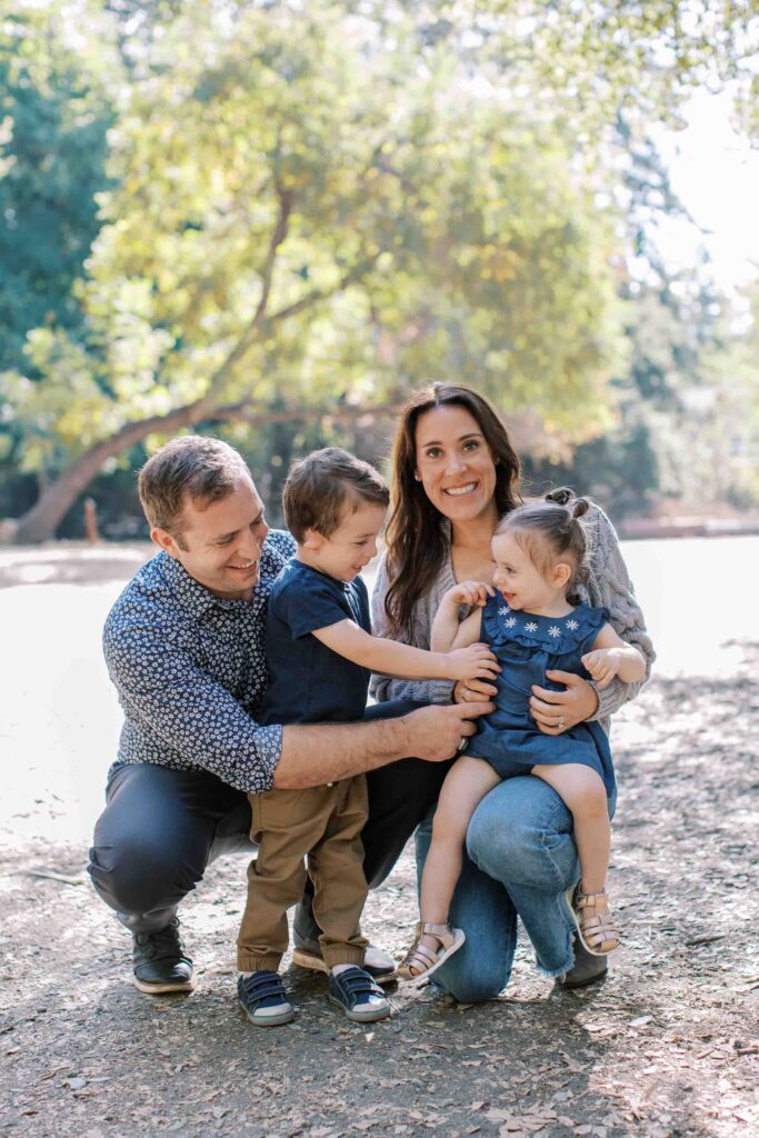 Smiling family of four kneeling and tickling each other lightheartedly