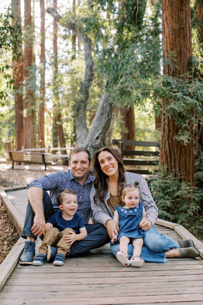 Smiling family of four sitting on a path between redwood trees