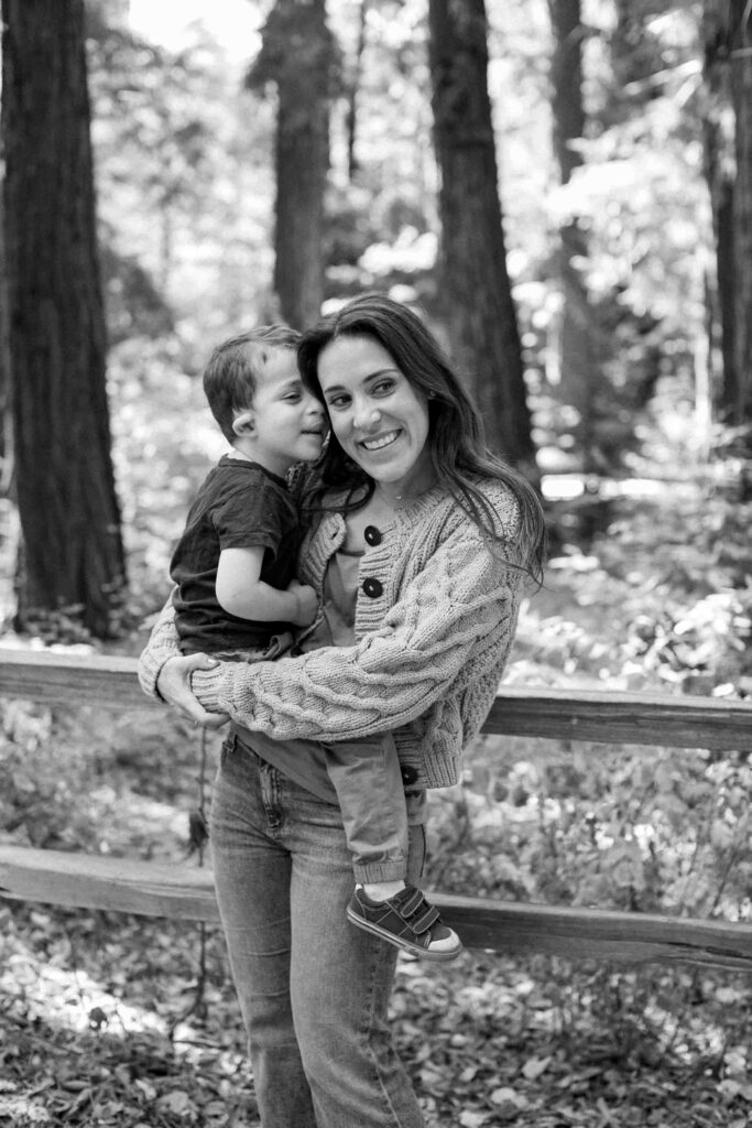 Mother holding and smiling at her young son in a wooded park