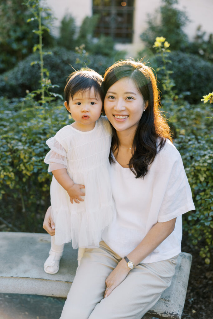 Mother and daughter sitting on a stone bench in neutral-colored outfits at Allied Arts Guild Menlo Park