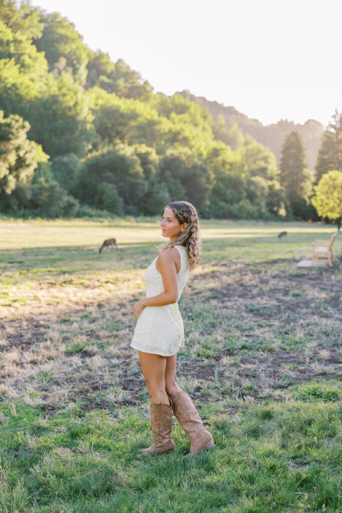 Teenage girl standing in an open meadow with deer wandering behind her